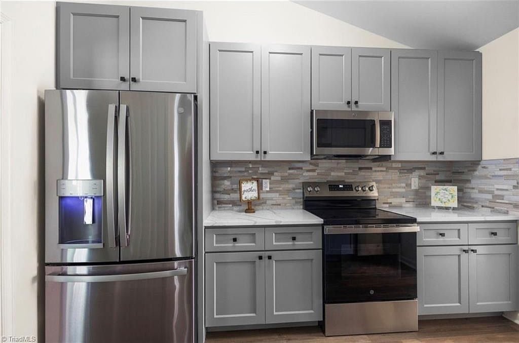 Kitchen after renovation with new cabinets, tile backsplash, and stainless appliances